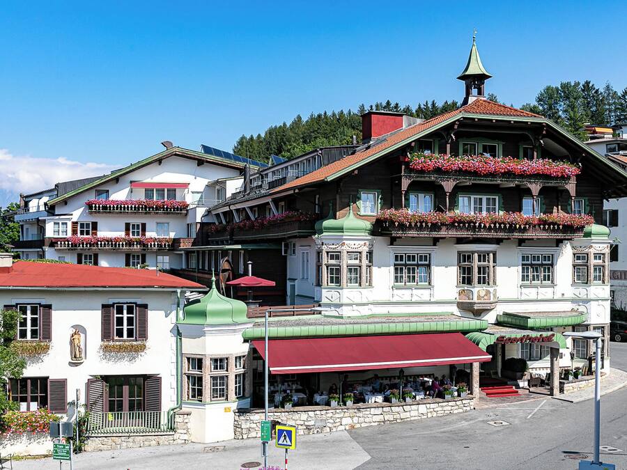 Ett traditionellt europeiskt hotell med flera våningar, balkonger med blomlådor och ett framträdande kyrktorn.