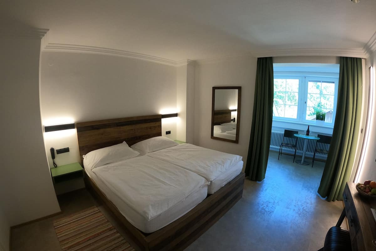 A hotel room with a double bed, bedside tables, a mirror, a view of the outdoors, and a small dining area.
