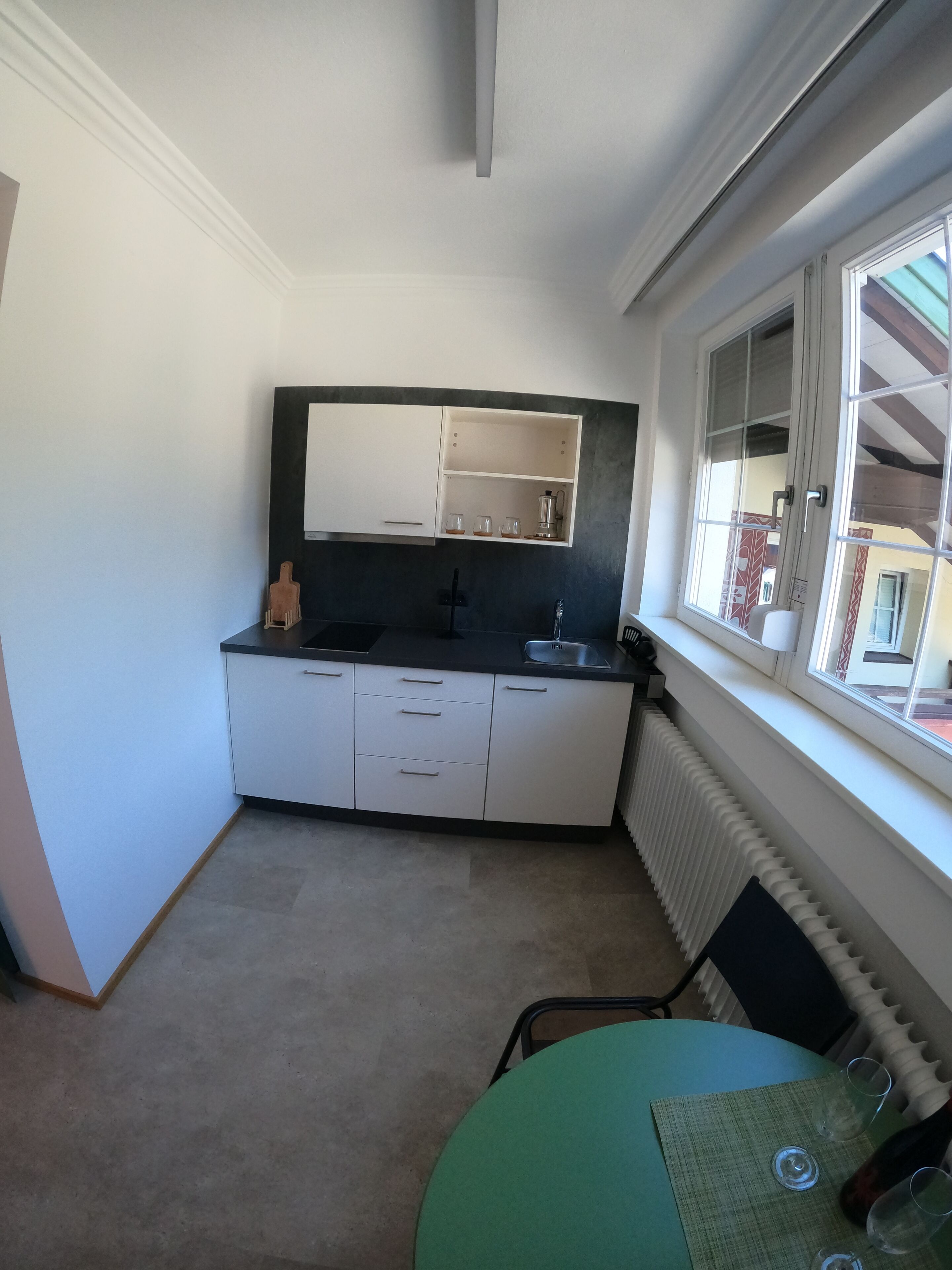 Cocina pequeña con ventana, radiador y una mesa con vasos.