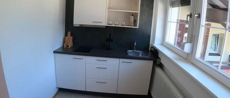 Cocina pequeña con ventana, radiador y una mesa con vasos.