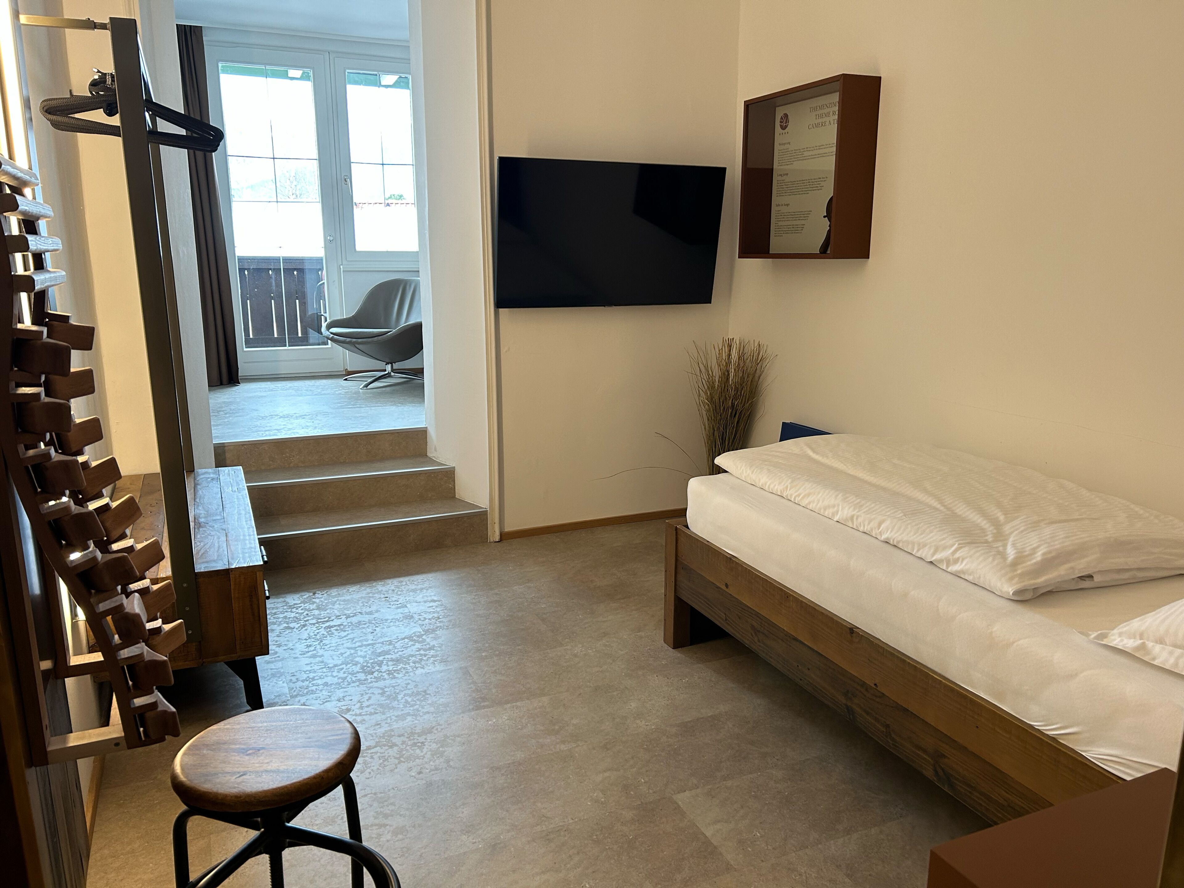 Un dormitorio con cama, televisor montado en la pared, banca y silla.