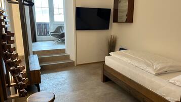 Ein Schlafzimmer mit einem Bett, einem an der Wand montierten Fernseher, einer Bank und einem Sessel.