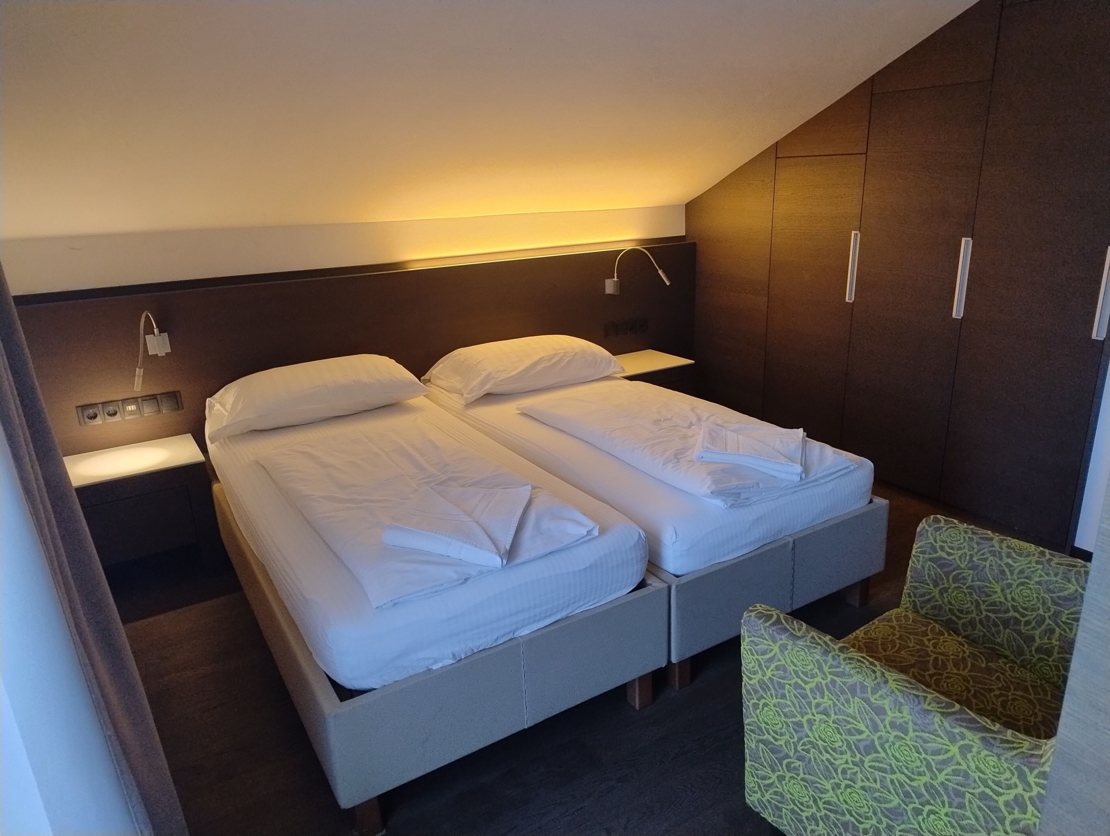 Une chambre d’hôtel avec un lit, une table de chevet, une lampe et un fauteuil à motifs.
