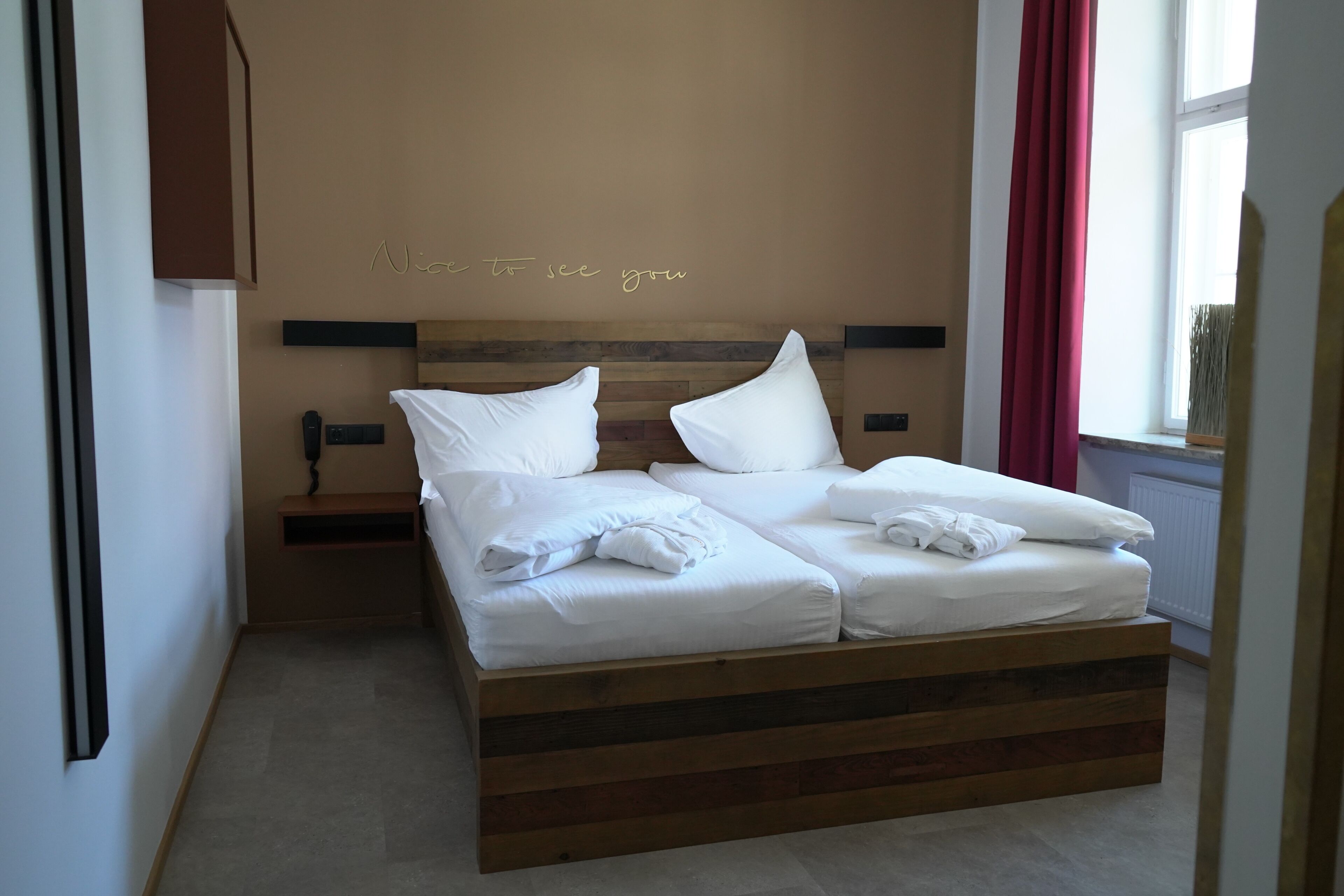 Una cama bien hecha con sábanas y almohadas blancas, un cabecero de madera y una mesita de noche con una lámpara.