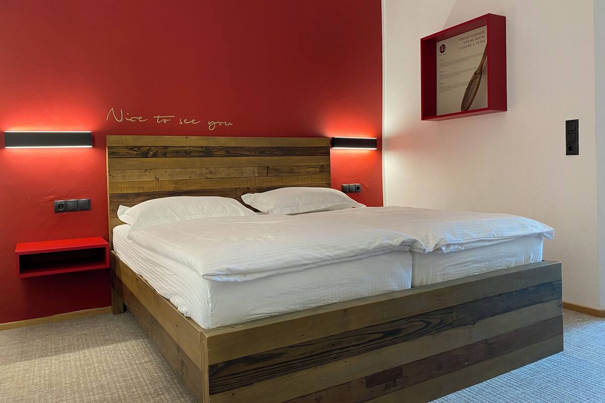 A neatly made bed with white linens, a wooden headboard, and two bedside tables with red accents.
