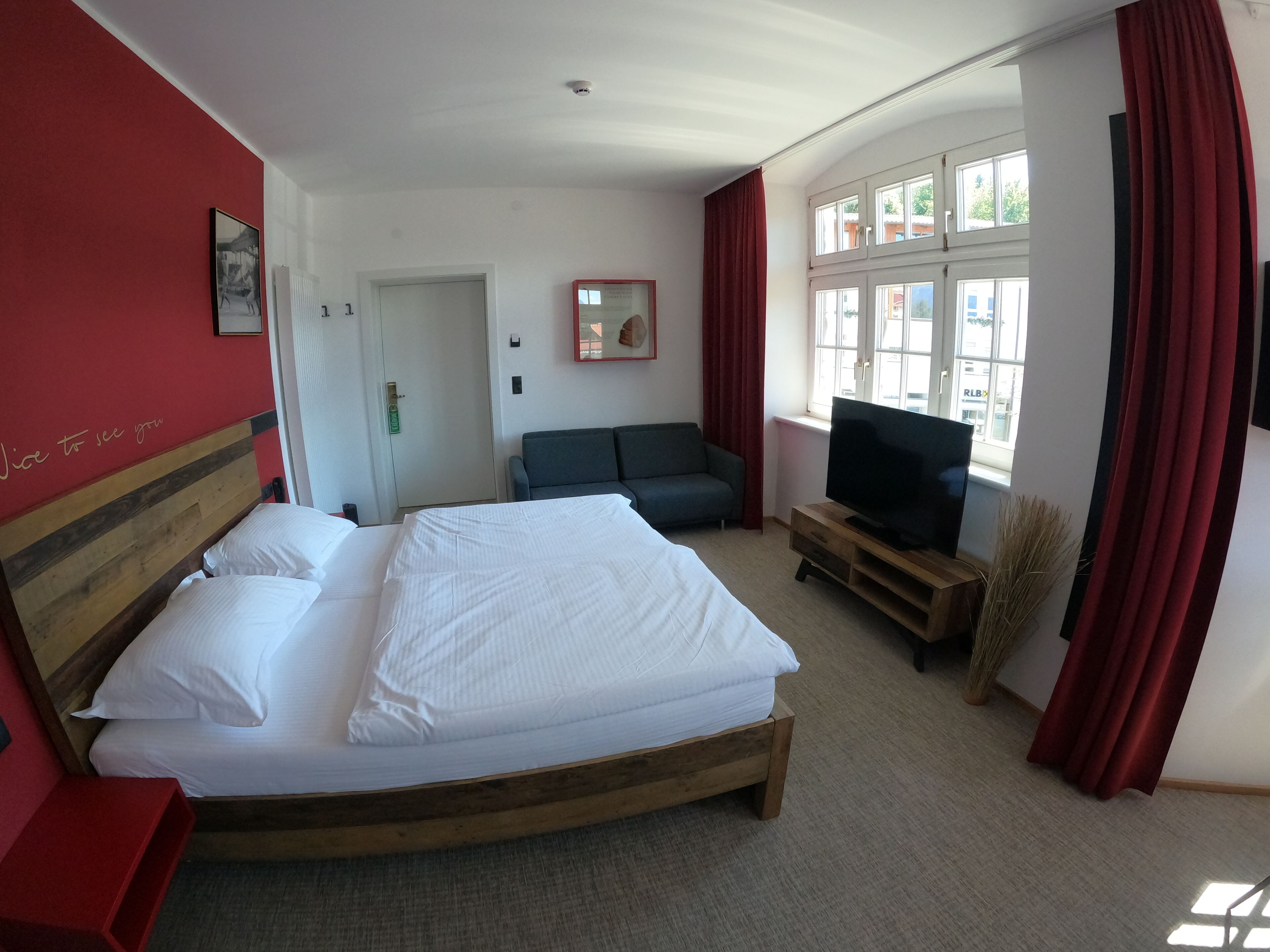 Ein Hotelzimmer mit einem großen Bett, einer Couch, einem Fernseher auf einem Holzständer und einem Fenster mit Vorhängen.