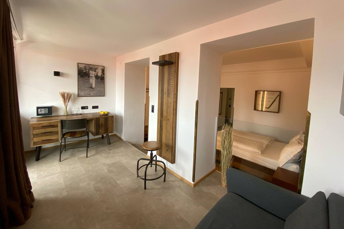 A modern hotel room with a desk, a chair, a bed, and a sofa.
