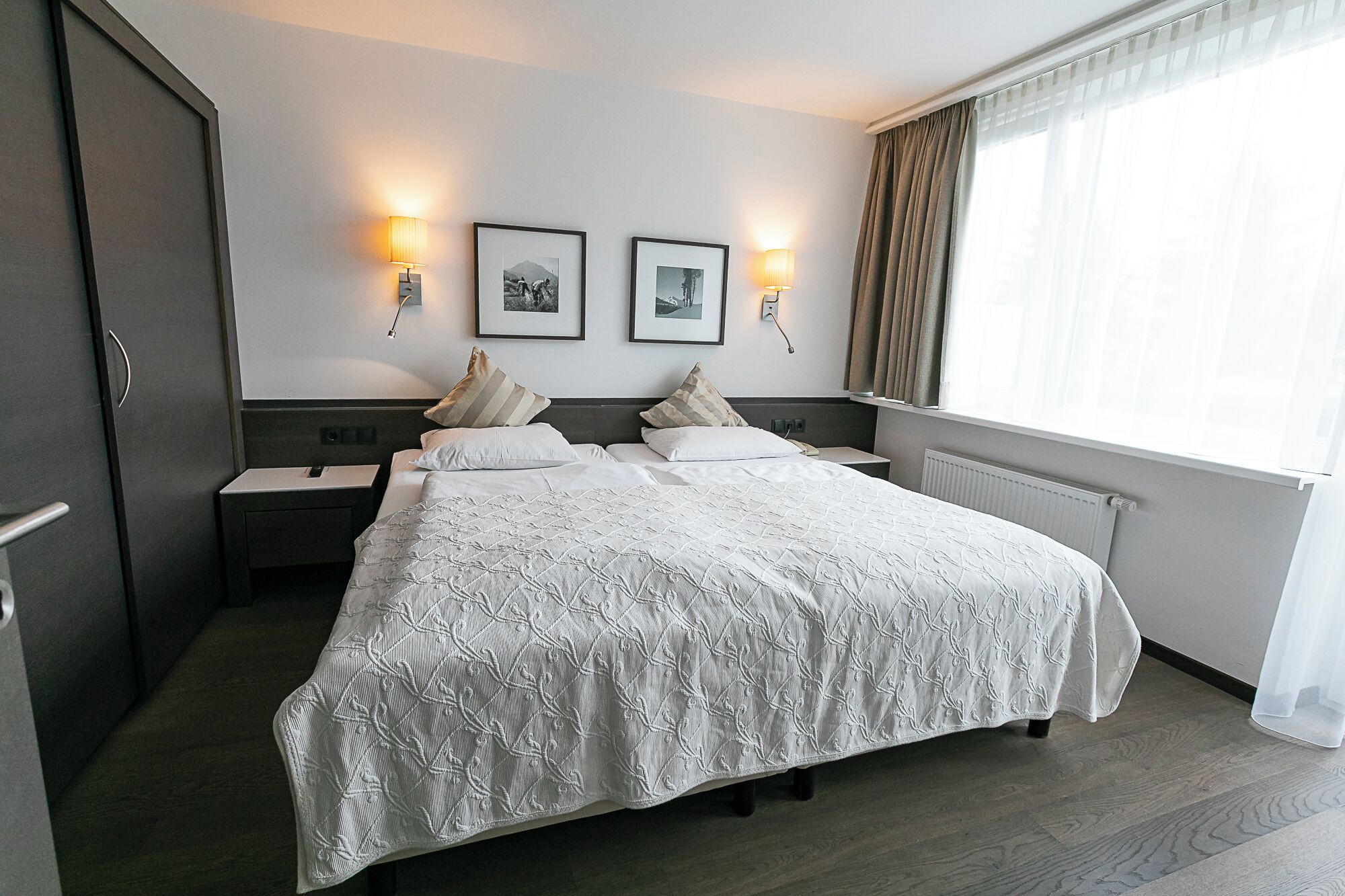 Een hotelkamer met een groot bed, twee nachtkastjes, een kledingkast en twee wandlampen.