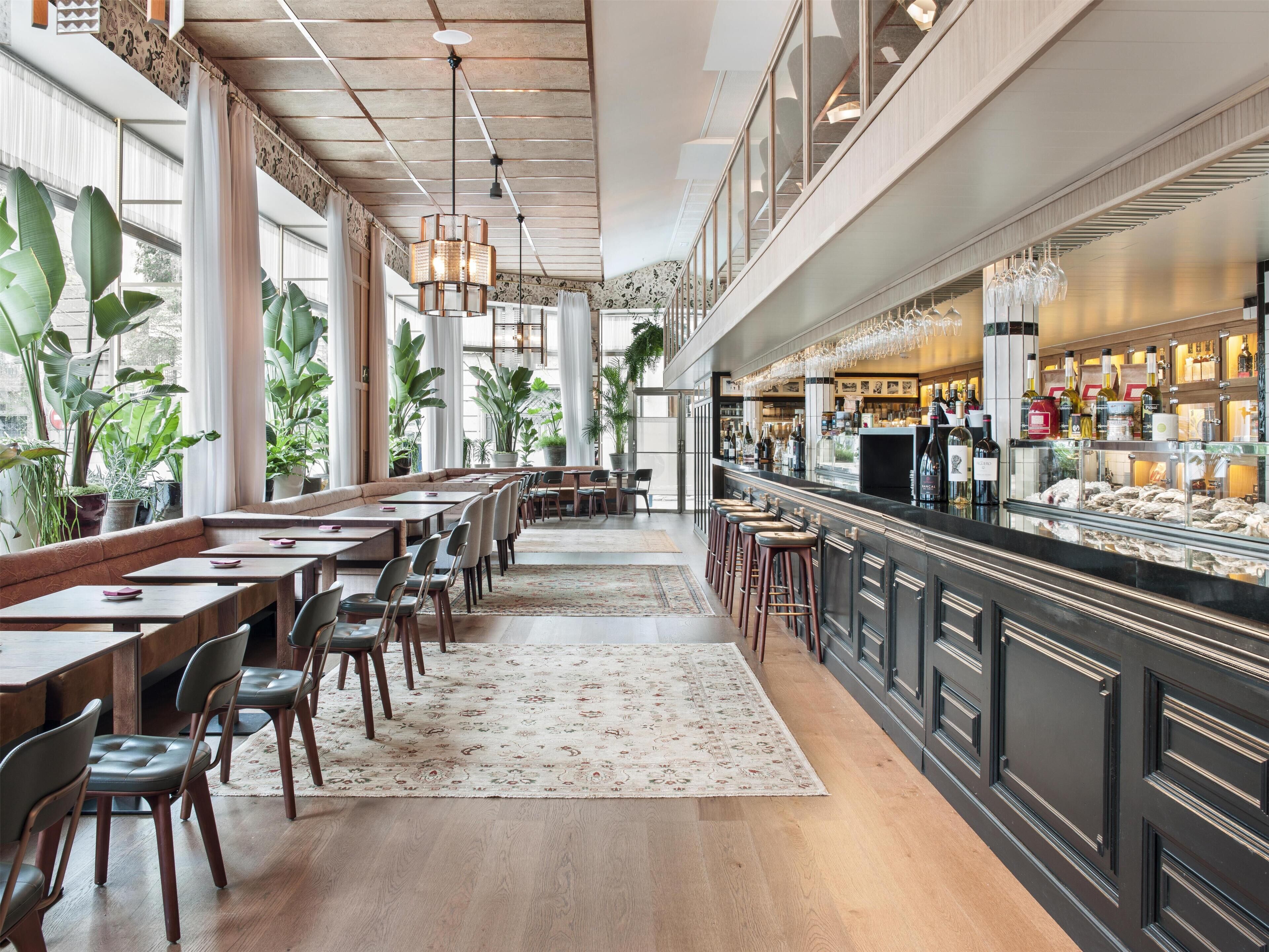 Ein geräumiges Restaurant mit hohen Decken, großen Fenstern und verschiedenen Sitzgelegenheiten, darunter Tische und Barhocker.
