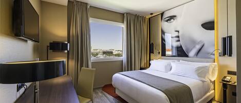 A modern hotel room with a large bed, a desk, a flat-screen TV mounted on the wall, and a window with curtains.