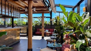 A modern outdoor seating area with wooden furniture, potted plants, and a bar counter. - NH Collection Madrid Suecia (Madrid)