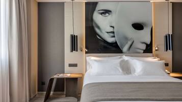 Una habitación de hotel moderna con una cama grande, una mesita de noche, una lámpara fijada a la pared y un cuadro abstracto de gran tamaño.