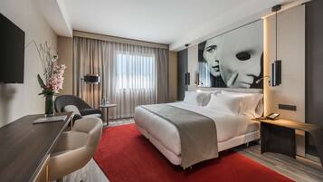 Ein modernes Hotelzimmer mit einem großen Bett, einem Schreibtisch mit Stuhl, einem roten Teppich und einem großen Fenster mit Vorhängen.