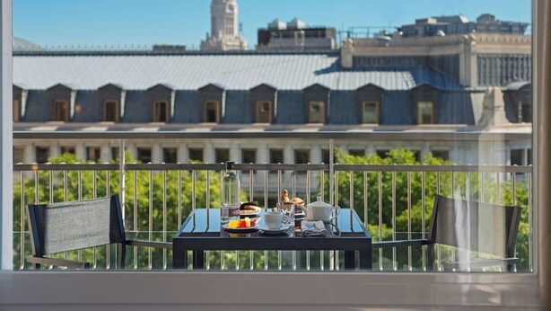 A balcony with a table set for breakfast, overlooking a row of buildings with a prominent tower. - NH Collection Madrid Suecia (Madrid)