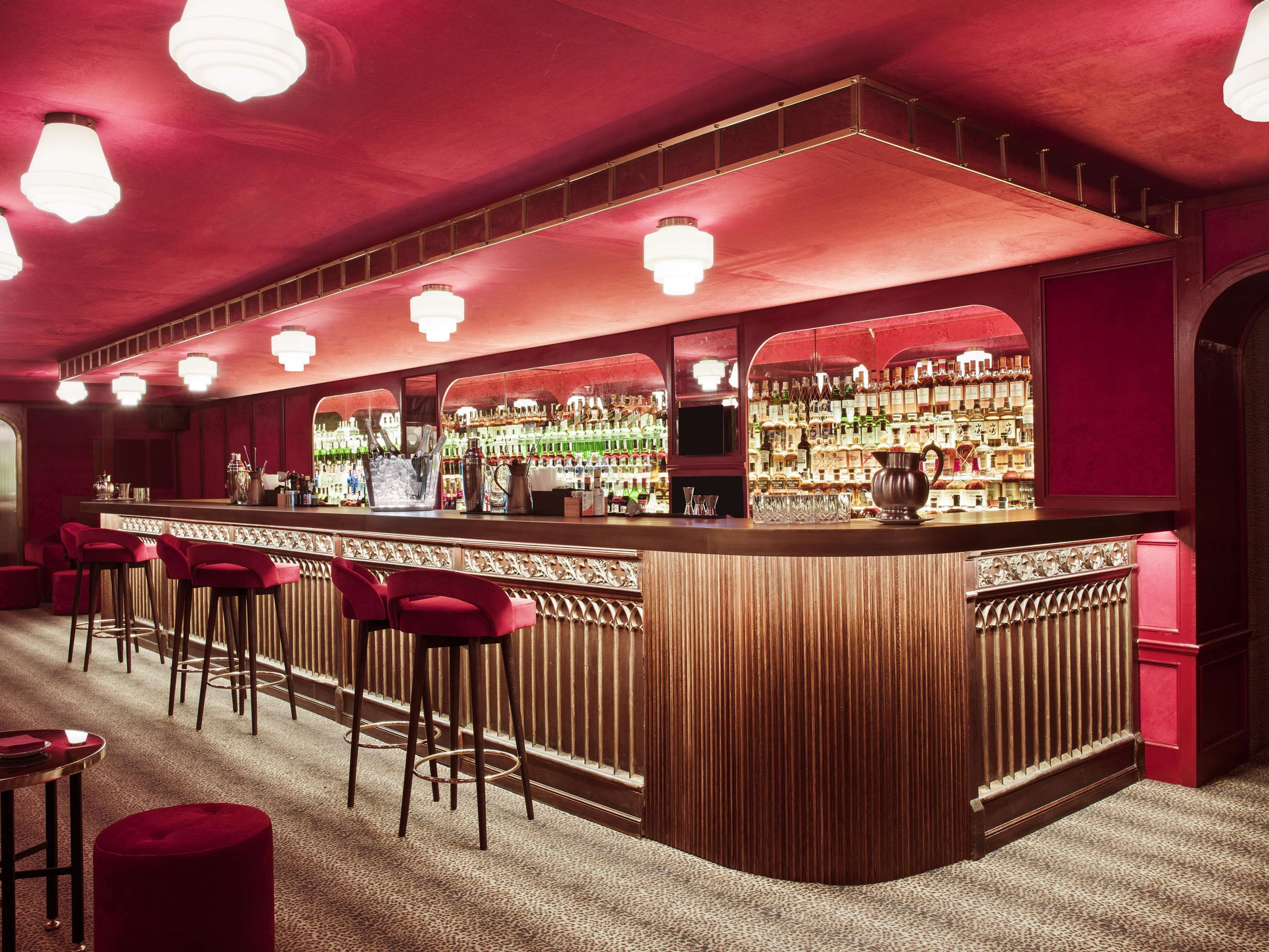 Zona de bar con mostrador de madera, taburetes rojos y estantes llenos de botellas.