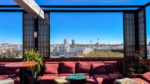 A rooftop terrace with a city view, red seating, and potted plants. - NH Collection Madrid Suecia (Madrid)