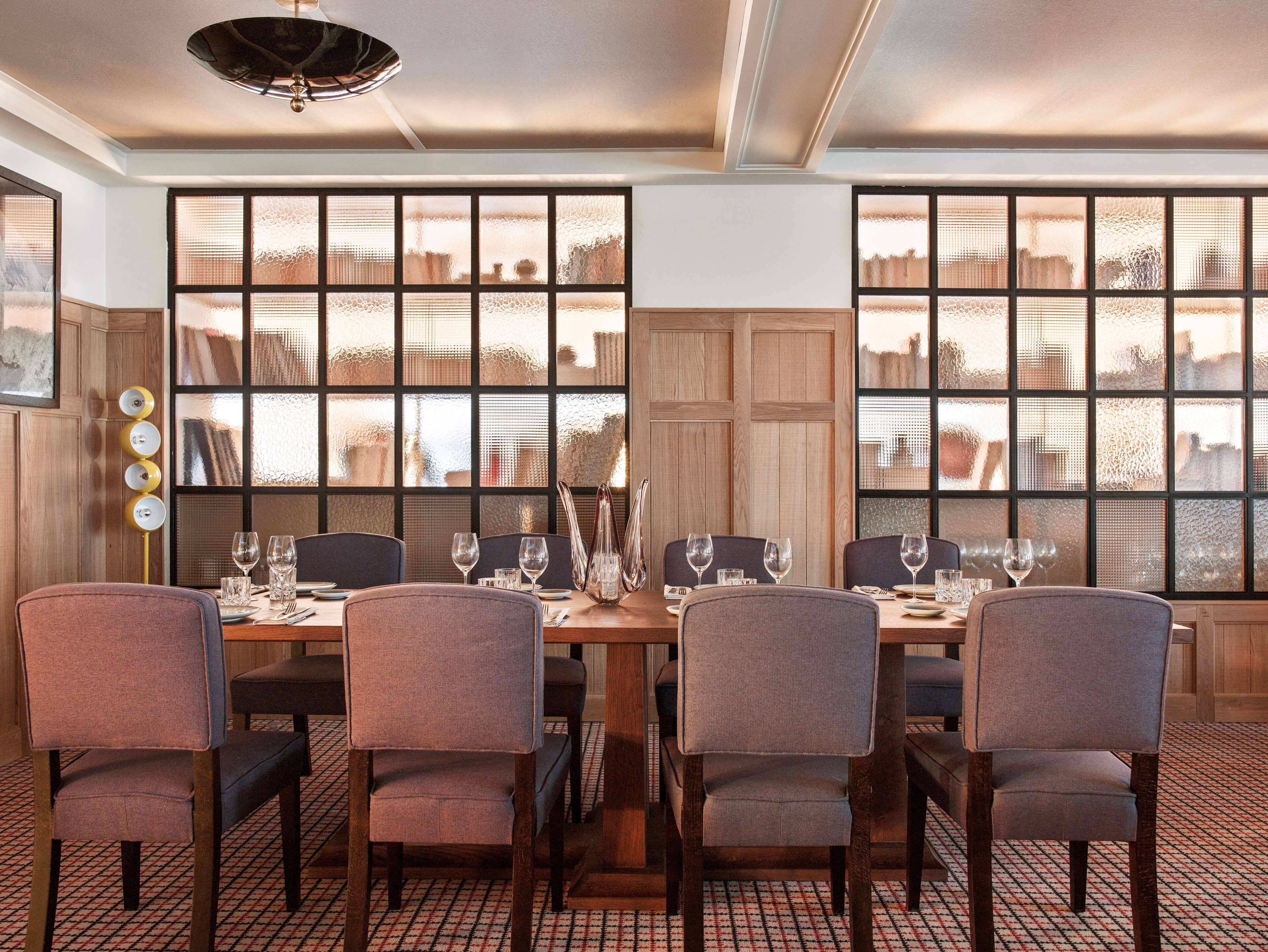 A dining area with a long table set for six, surrounded by chairs, with a decorative light fixture above.
