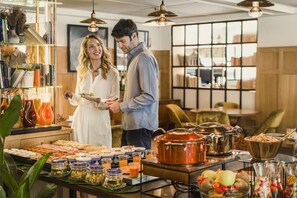 A buffet setup with various food items and a man and woman standing by the counter. - NH Collection Madrid Suecia (Madrid)