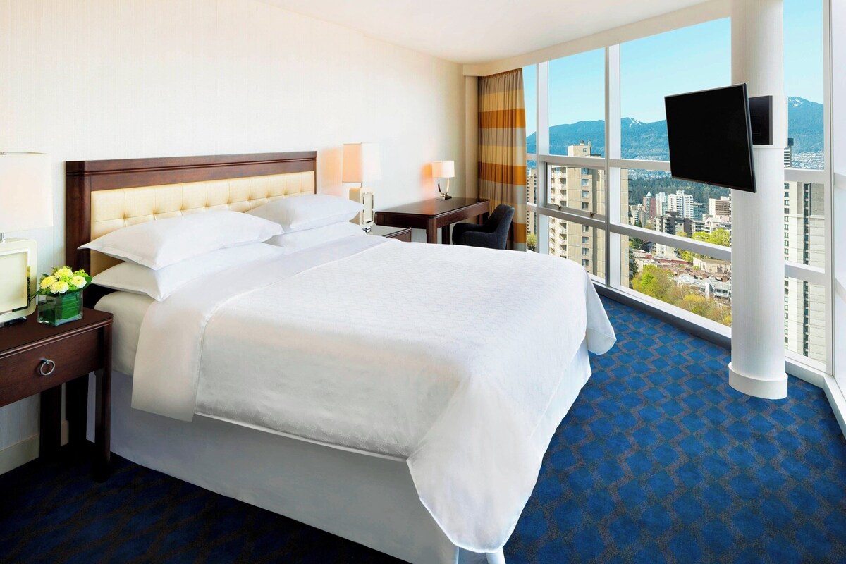 Quarto de hotel com uma cama grande, uma escrivaninha, uma cadeira e uma televisão.