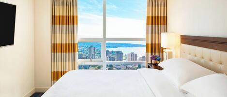 A hotel room with a large bed, a TV on the wall, and a view of the city through the window.