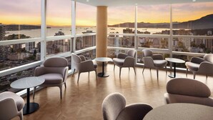Un salón moderno con varias zonas de estar, amplios ventanales con vistas a la ciudad y un suelo de madera con patrón de espiga.