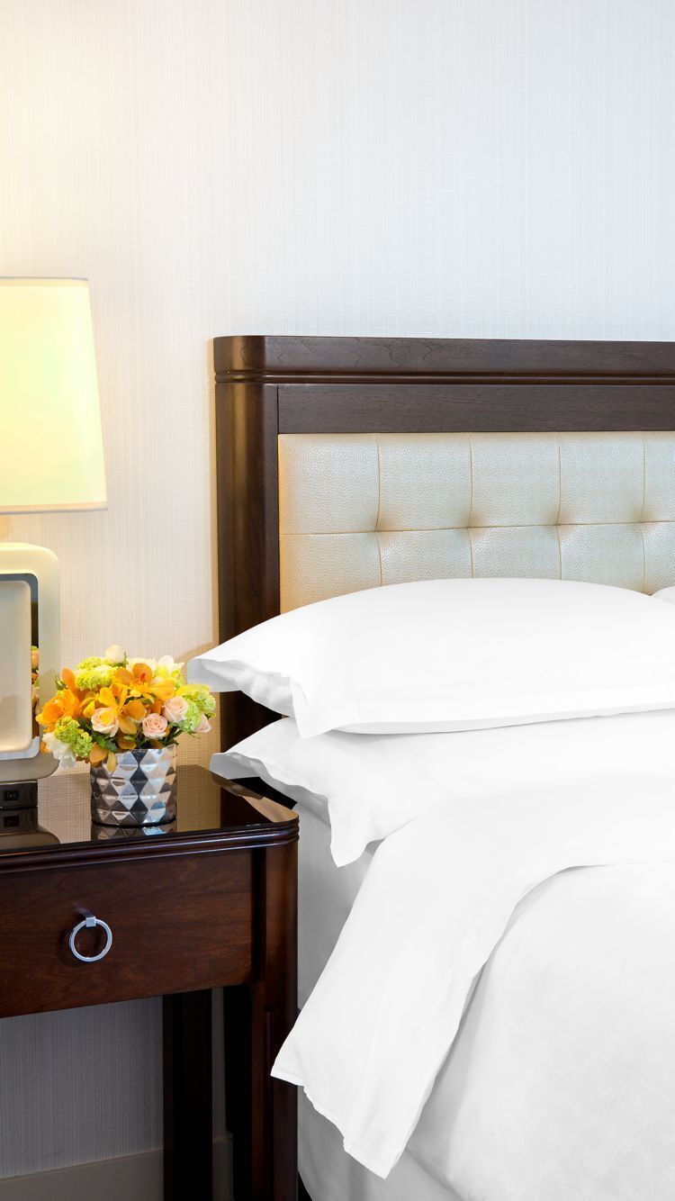 A hotel room with a bed, a nightstand, a lamp, and a vase with flowers.