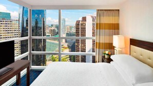 Habitación de hotel con un ventanal grande, una cama, una mesita de noche, una lámpara y un televisor.