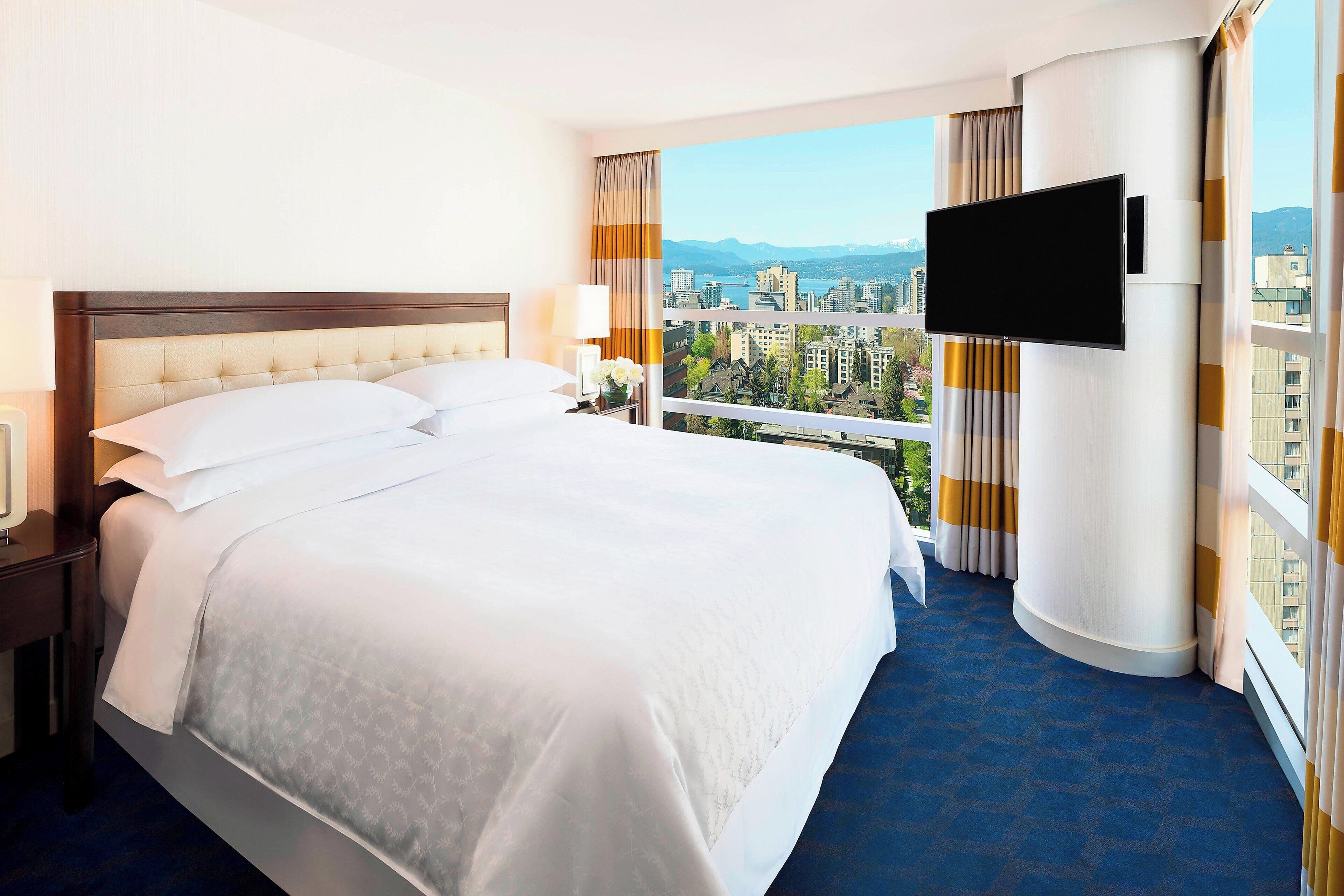 A hotel room with a large bed, a TV mounted on the wall, and a balcony with a city view.