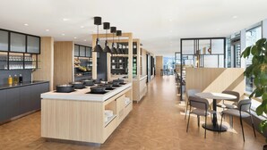A modern kitchen with a central island, dining area with tables and chairs, and a view of the city through large windows. - Sheraton Vancouver Wall Centre (Vancouver)