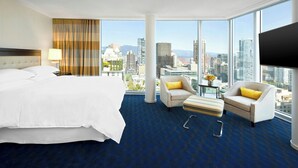 Habitación de hotel con una cama grande, dos sillones, una mesita y vistas a la ciudad.