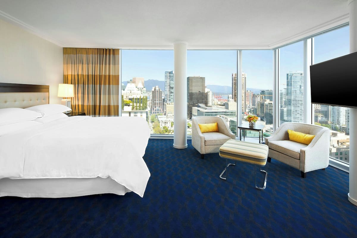 Habitación de hotel con una cama grande, dos sillones, una mesita y vistas a la ciudad.