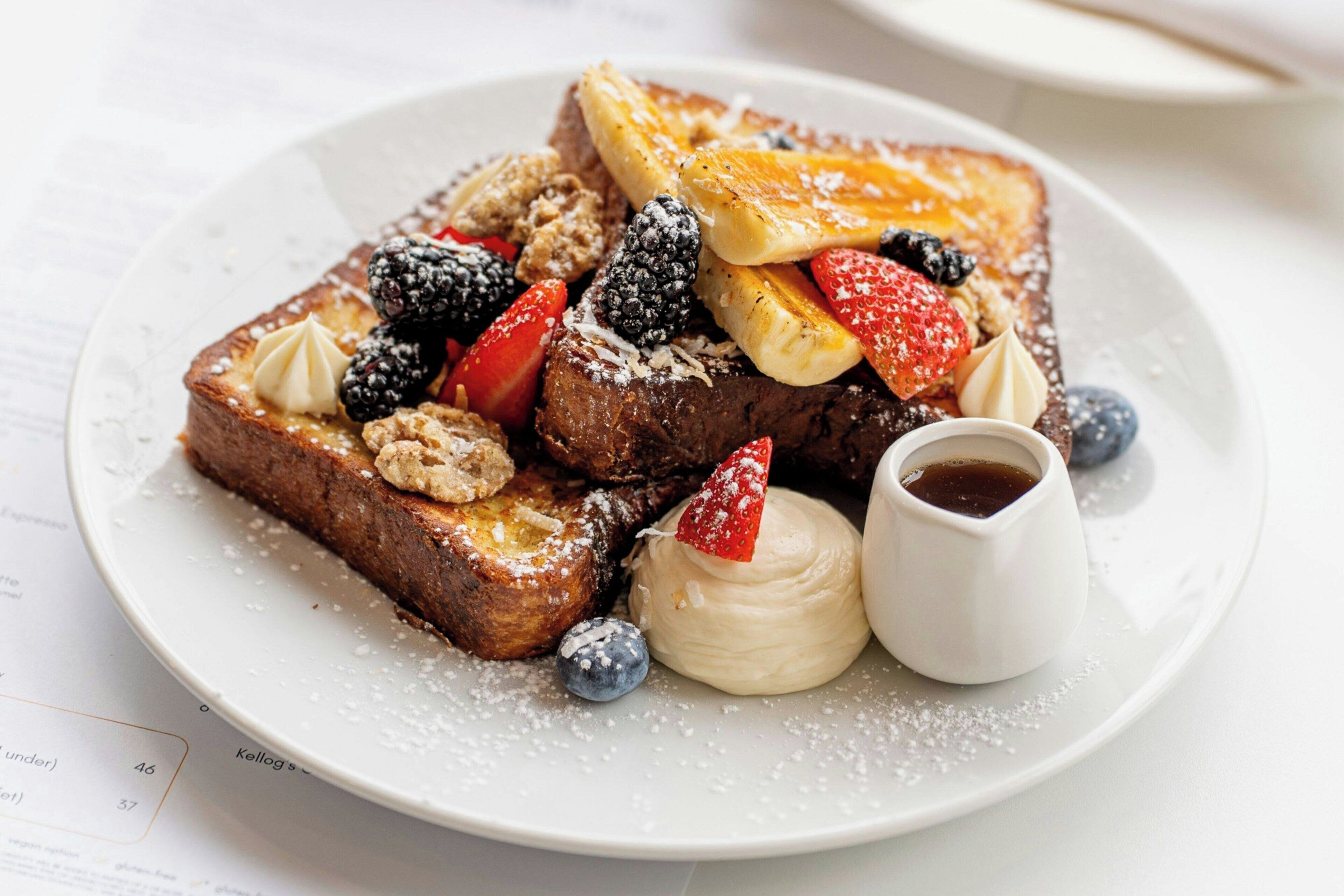 A plate of French toast with berries, whipped cream, and syrup.