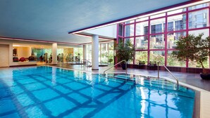 Una piscina interior con agua cristalina y azul, rodeada de amplios ventanales y plantas de interior.