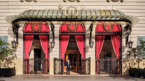 Un edificio con balcones ornamentales, una entrada imponente con cortinas rojas y un empleado uniformado en la puerta.