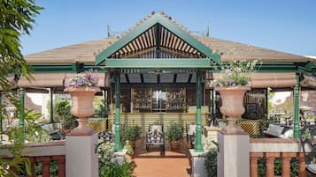 Un edificio tradicional con techo verde, entrada central con frontón triangular y plantas en macetas alrededor del acceso.