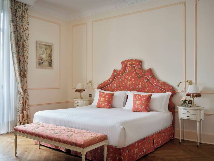 A bedroom with a large bed, two bedside tables, a bench, and a painting on the wall.