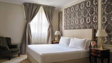 A neatly arranged hotel room with a large bed, two bedside tables with lamps, a chair, and patterned wallpaper.