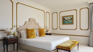 Una habitación de hotel con una cama grande, una mesita de noche con lámpara, un banco y un cuadro en la pared.