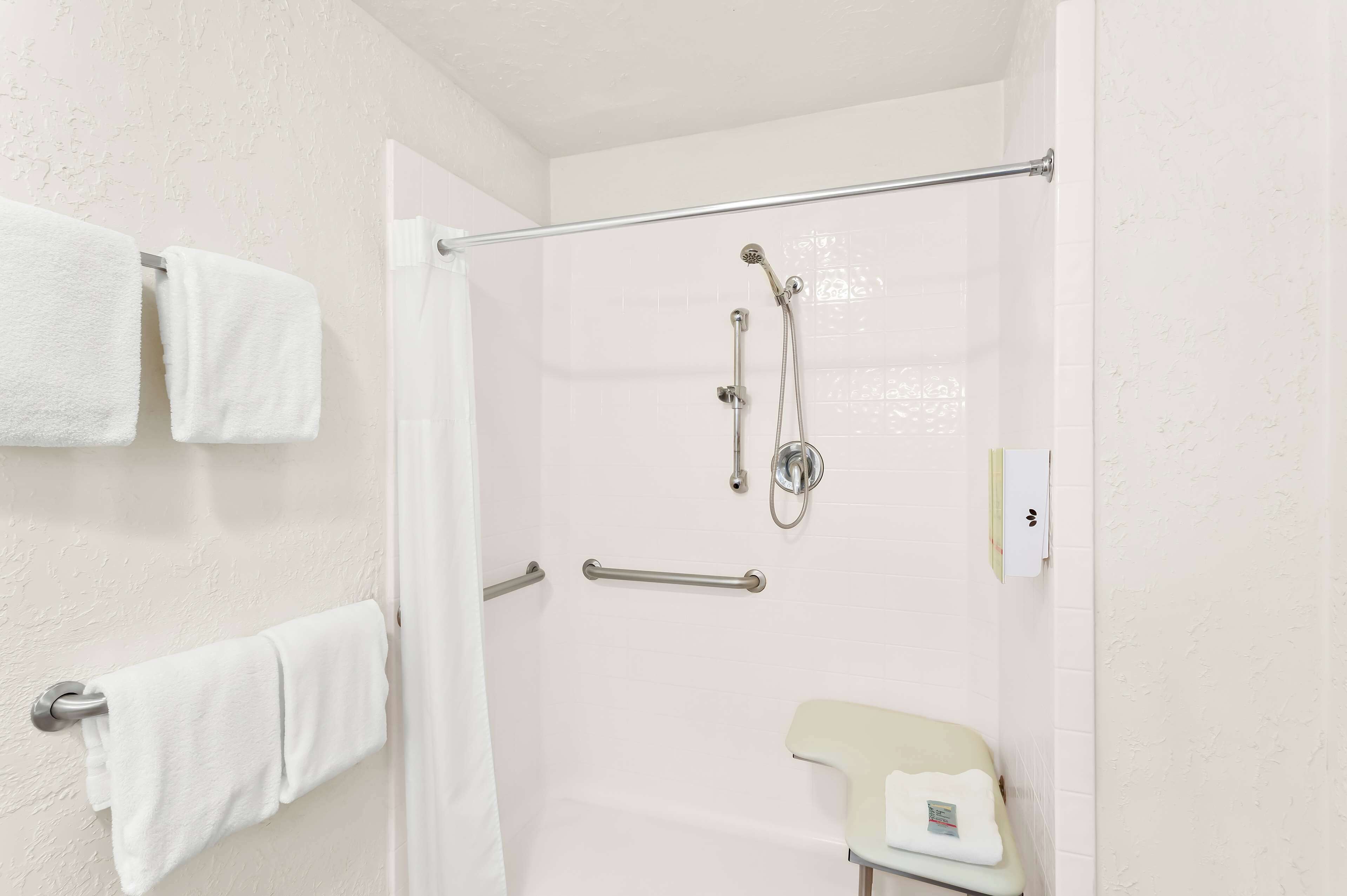 A shower area with a glass door, a towel rack with two towels, a handheld showerhead, and a handheld shower attachment.