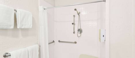 A shower area with a glass door, a towel rack with two towels, a handheld showerhead, and a handheld shower attachment.