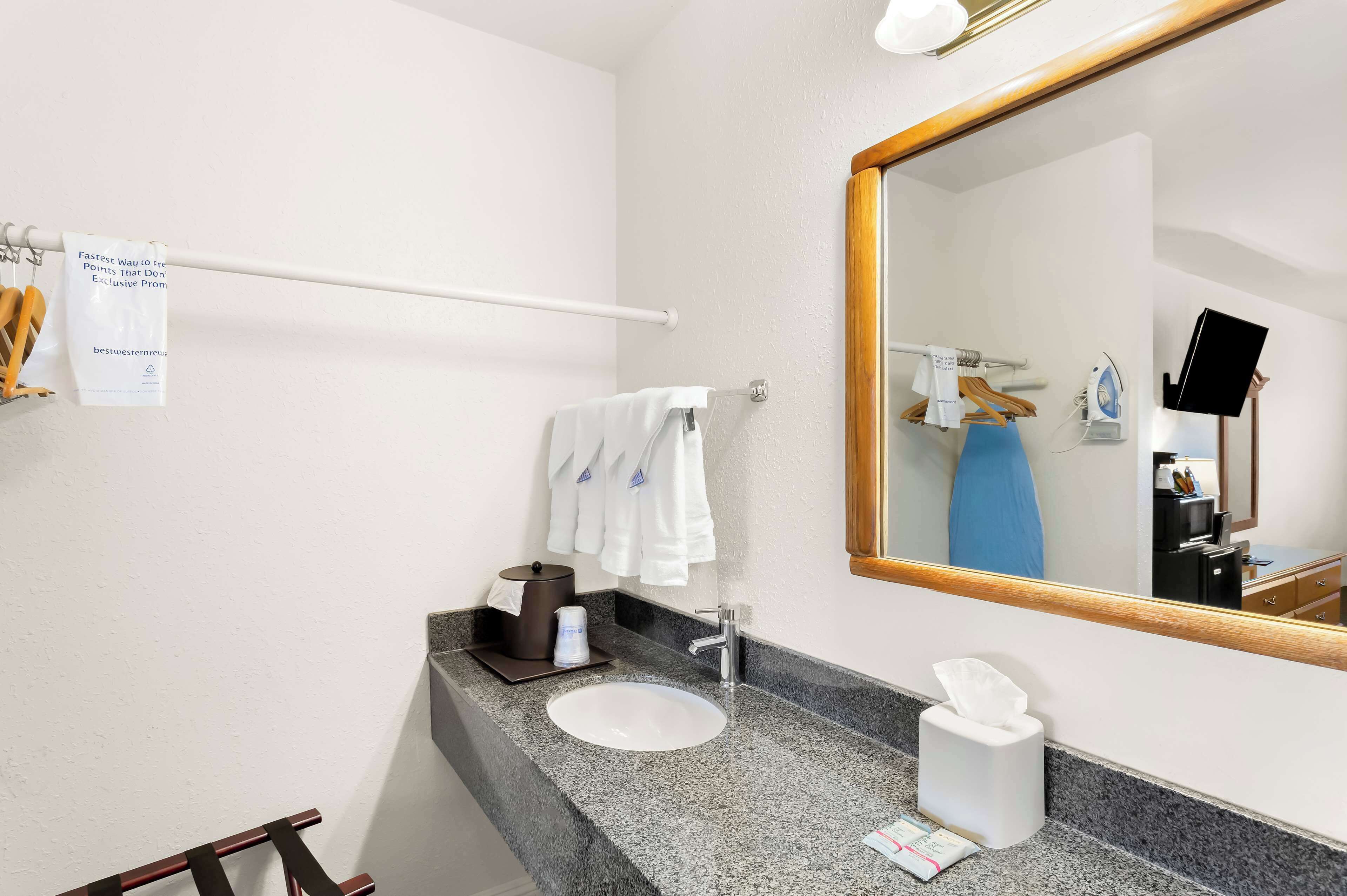 Une salle de bain d’hôtel avec un comptoir en granit, un lavabo, un miroir, un porte-serviettes et une serviette qui y est suspendue.
