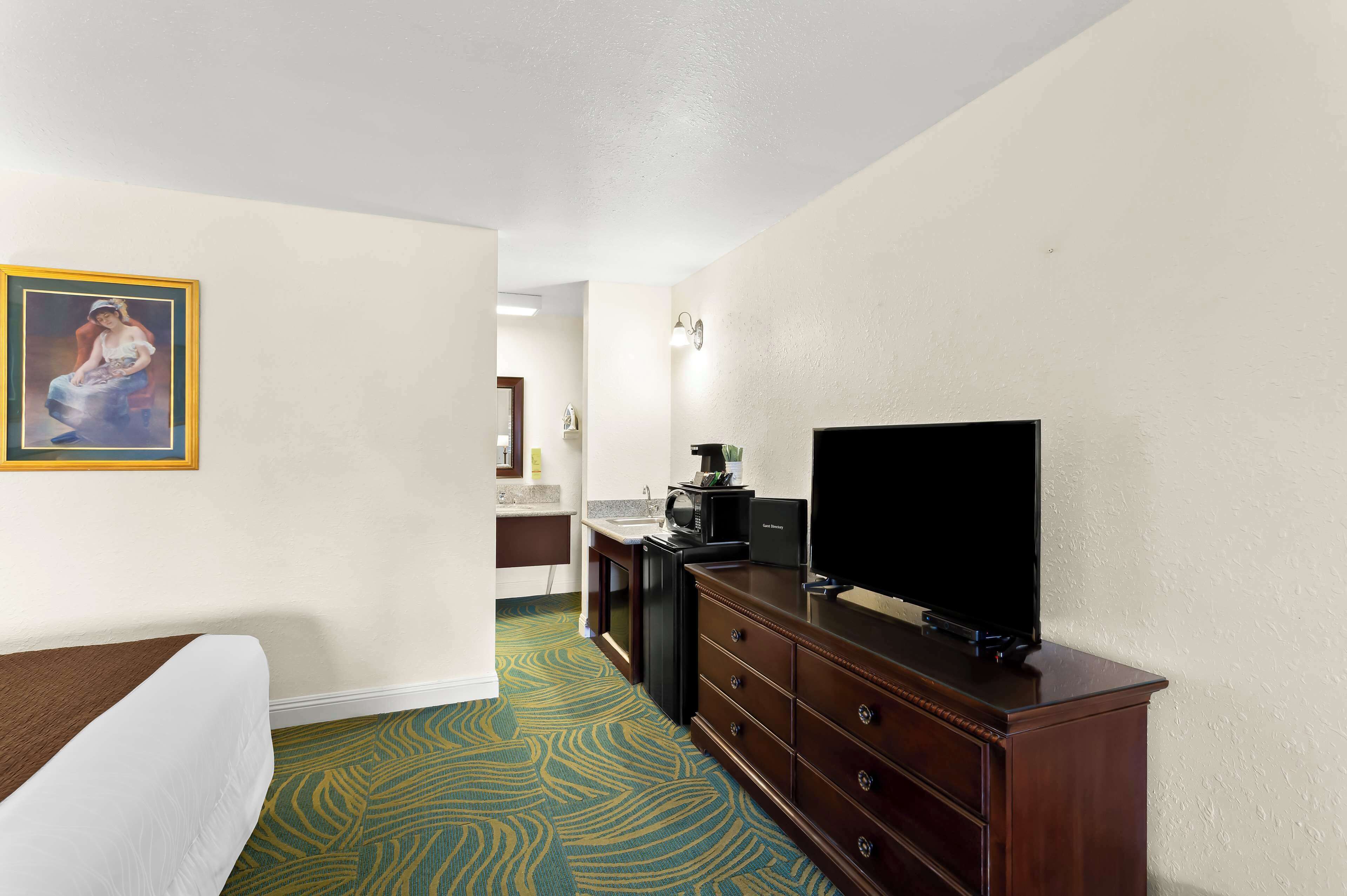 A hotel room with a bed, a dresser with a flat-screen TV, a microwave, and a sink.