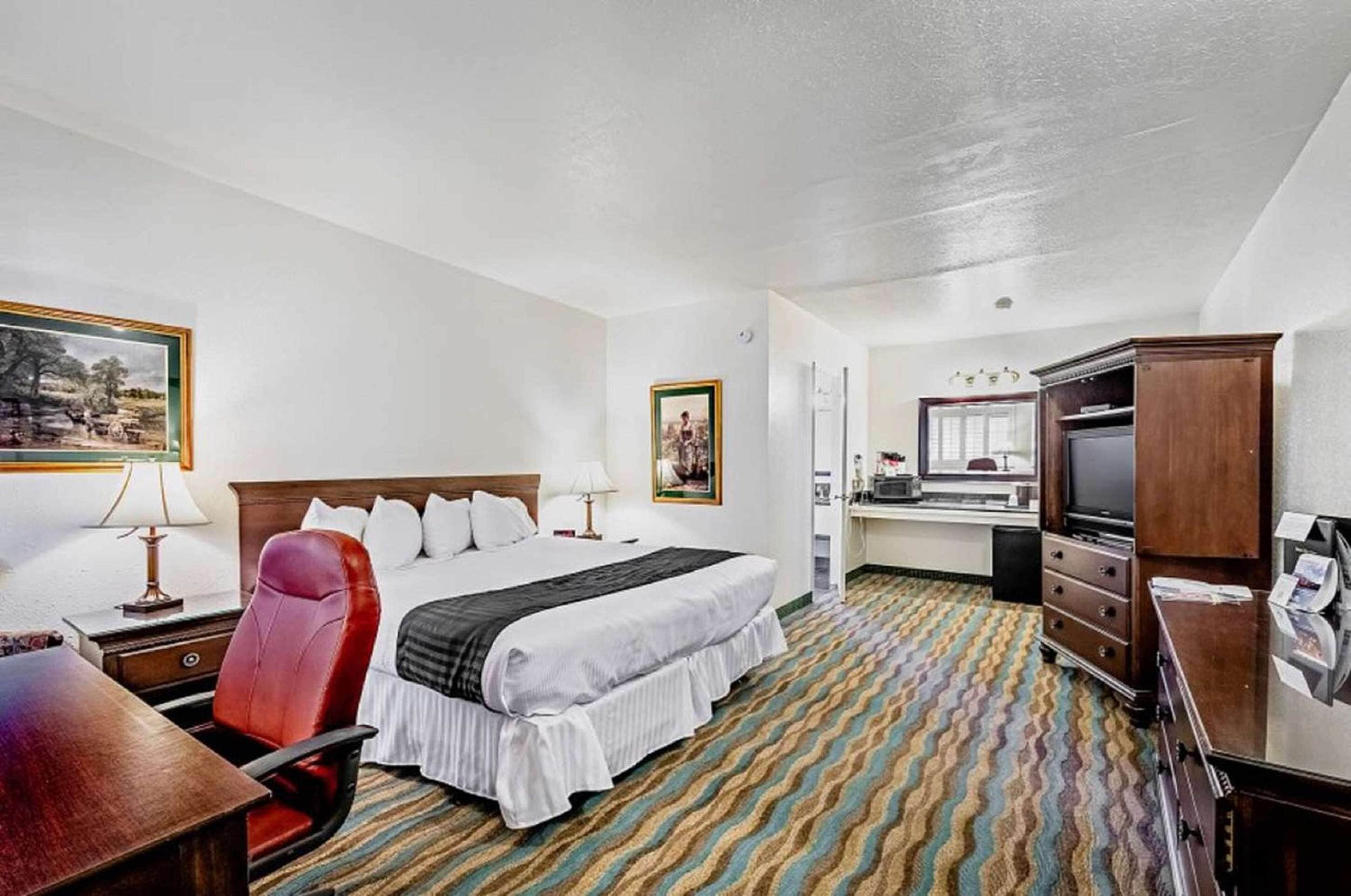 A hotel room with a bed, a desk, a chair, a television, and a wardrobe.