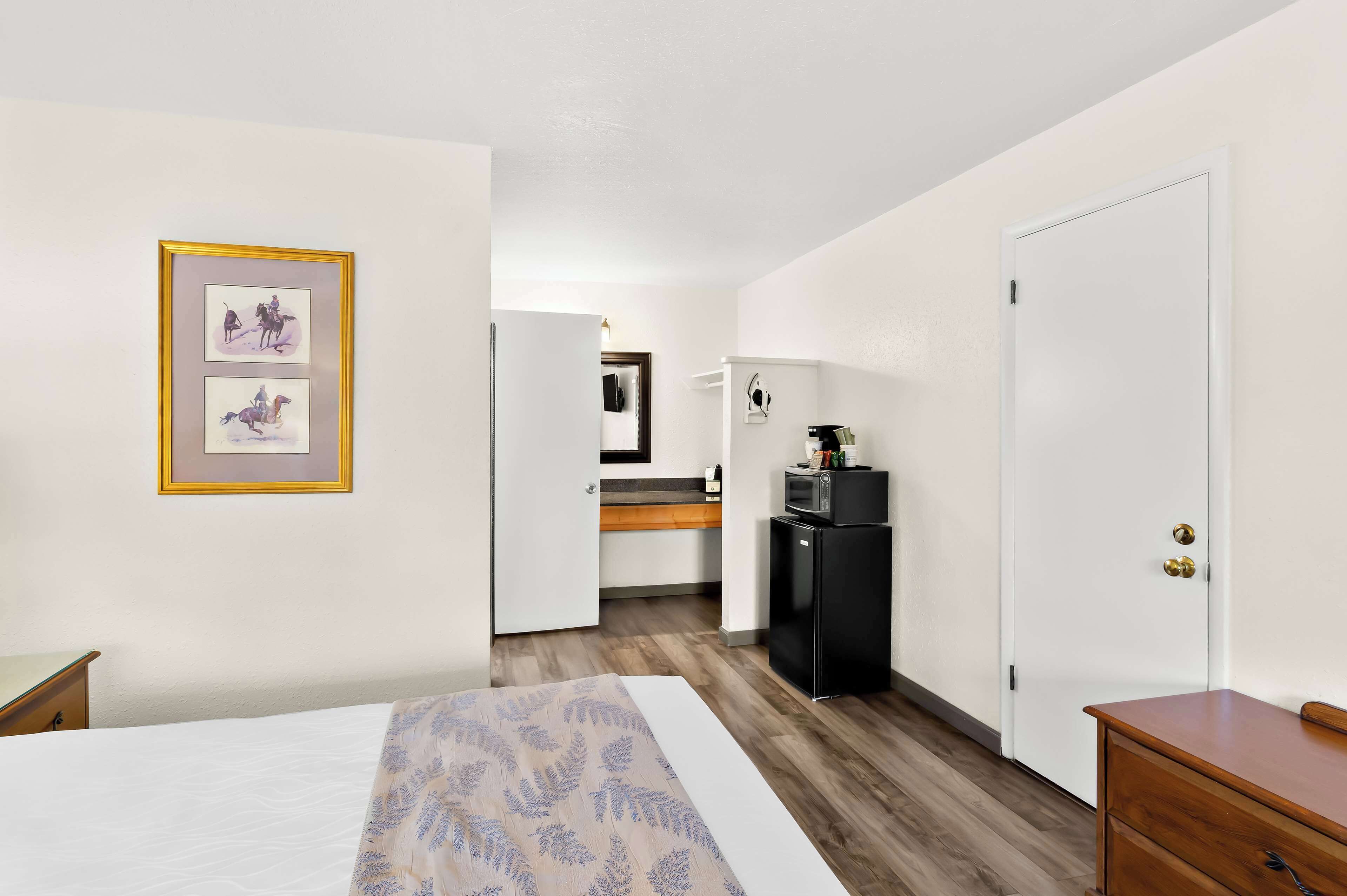 A hotel room with a bed, a desk, a small kitchenette, and a door.