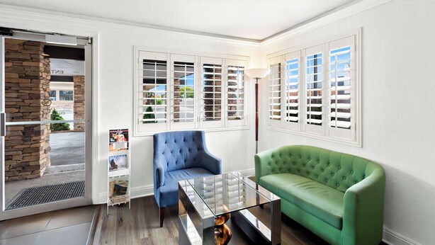 Una habitación de esquina con pared de piedra, un sillón azul, un sofá verde y una mesa de centro de vidrio.