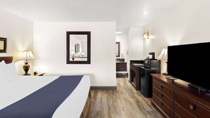 Una habitación de hotel con una cama, televisor de pantalla plana, cómoda y una pequeña kitchenette.