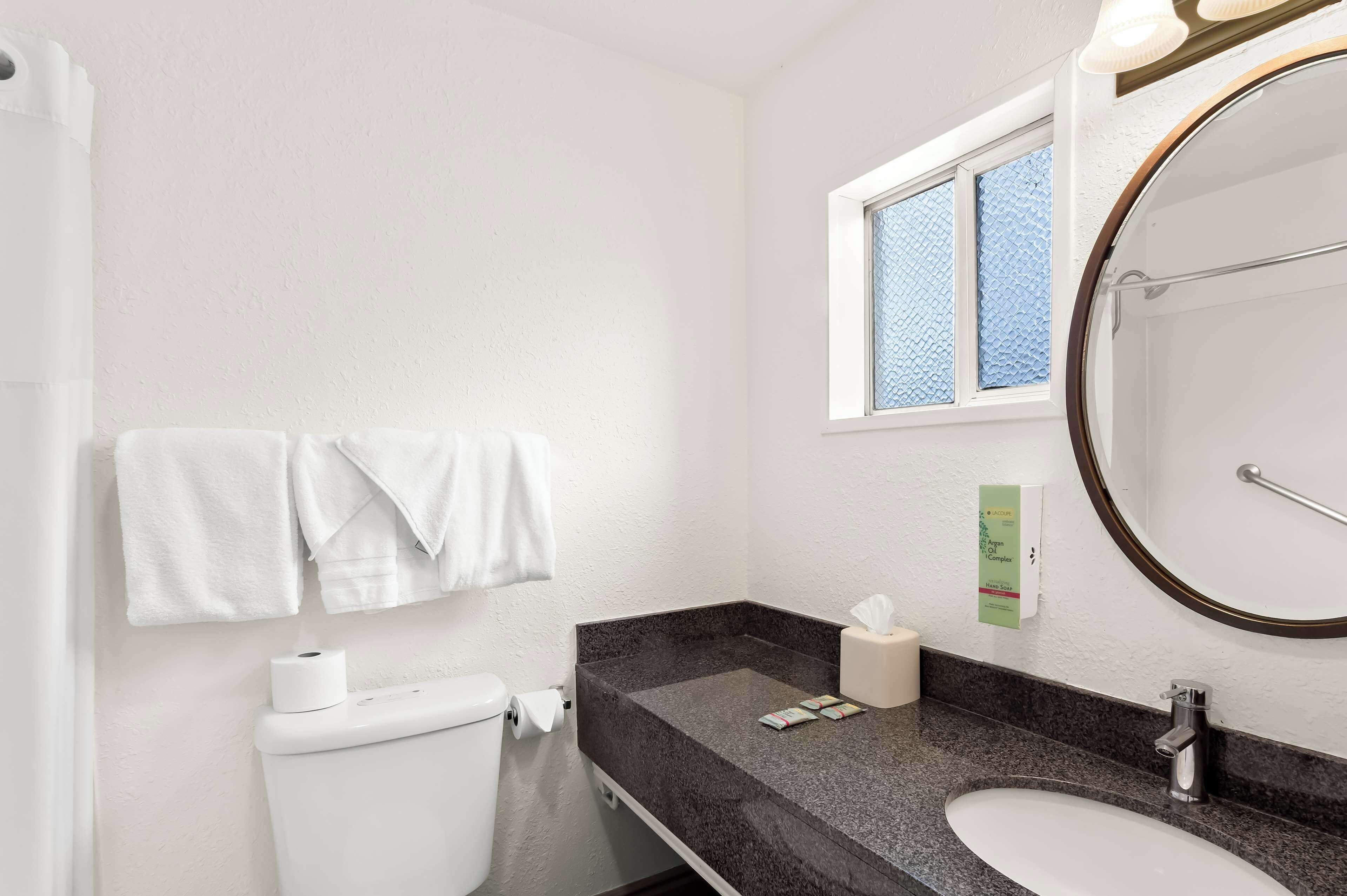A bathroom with a white toilet, a sink with a dark countertop, a mirror, and a window above the sink.