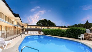 Una piscina con sillas de descanso y un edificio al fondo.