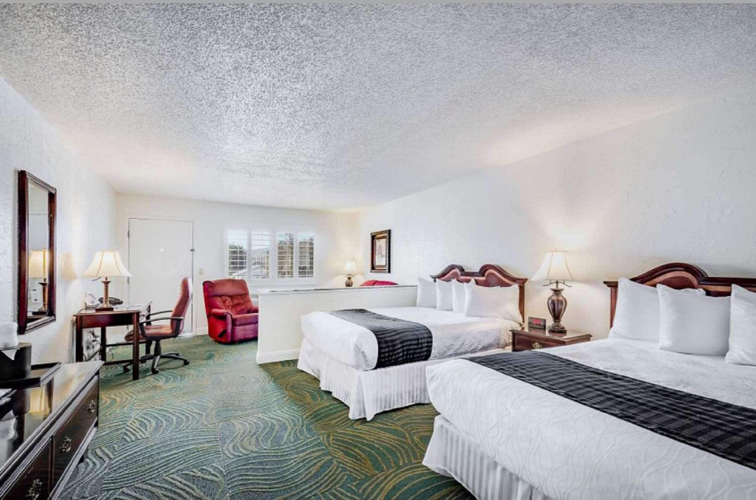 A hotel room with two beds, a desk, a chair, and a large window.