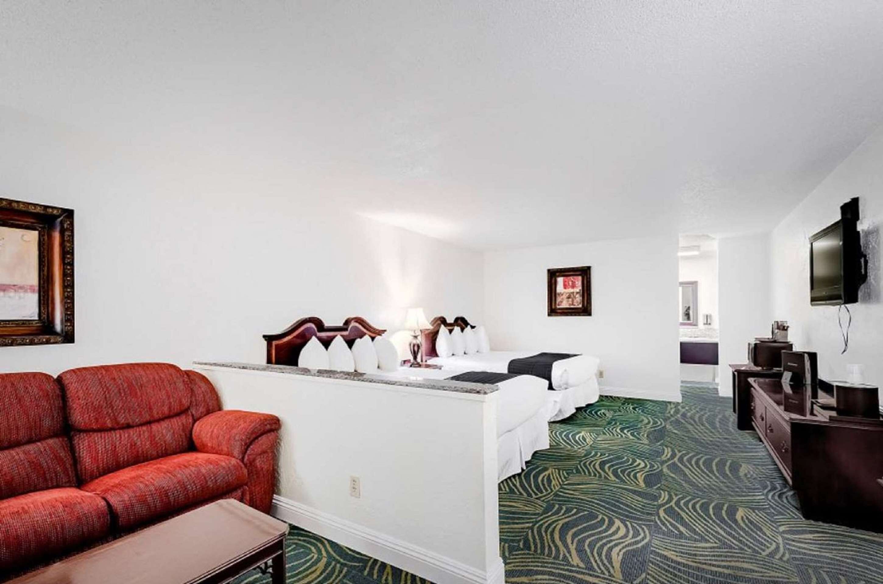 A hotel room with a sofa, two beds, a desk, and a TV.